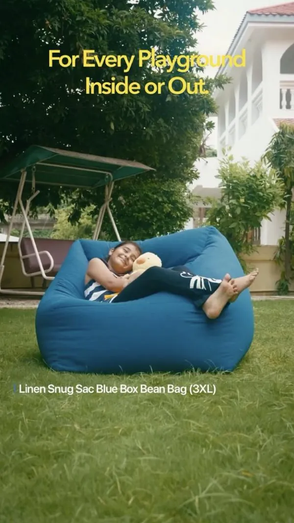 A child hugs a soft toy in a big blue bean bag out on the lawn.